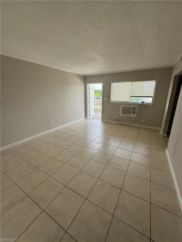Unfurnished room with a textured ceiling, a wall mounted AC, light tile patterned floors, and baseboards
