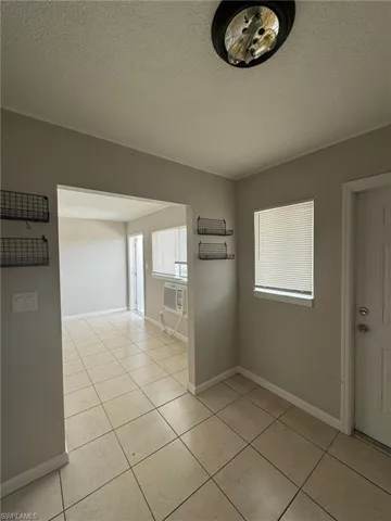 Unfurnished room featuring light tile patterned floors, baseboards, a textured ceiling, and an AC wall unit