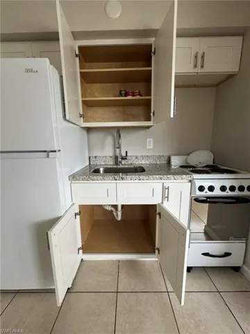 Kitchen with white appliances, a sink, white cabinetry, and light tile patterned flooring