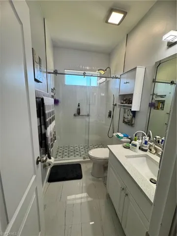 Bathroom with marble finish floor, toilet, a stall shower, and vanity