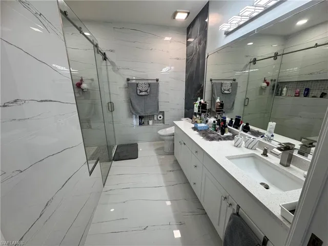 Bathroom with a shower stall, marble finish floor, toilet, and vanity