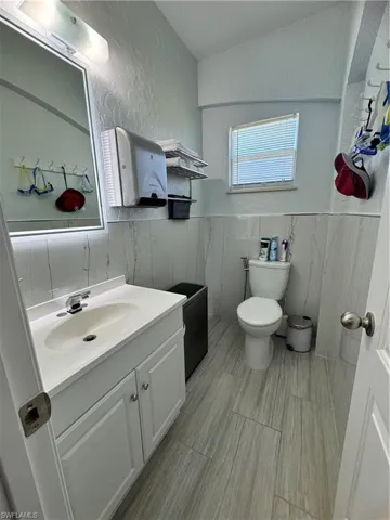 Bathroom featuring a wainscoted wall, a textured wall, toilet, vanity, and tile walls