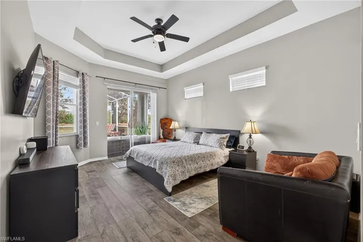 Bedroom featuring access to exterior, a tray ceiling, wood finished floors, and a ceiling fan