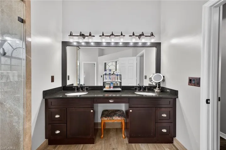 Bathroom featuring double vanity, light wood-type flooring, and a stall shower
