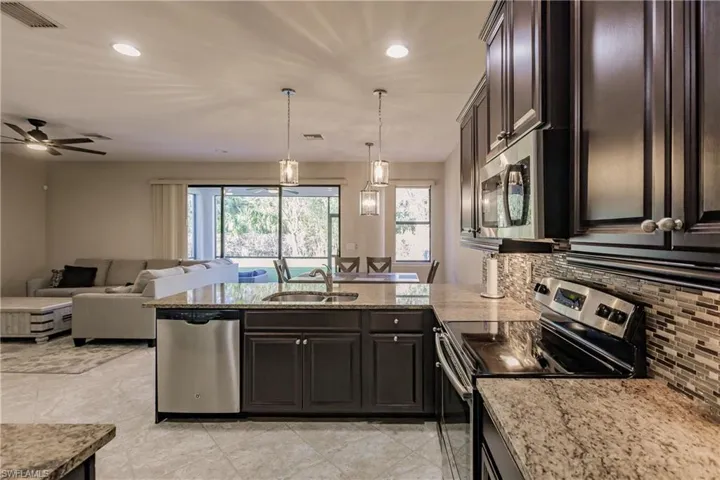 Kitchen featuring ceiling fan, appliances with stainless steel finishes, hanging light fixtures, dark brown cabinetry, and sink