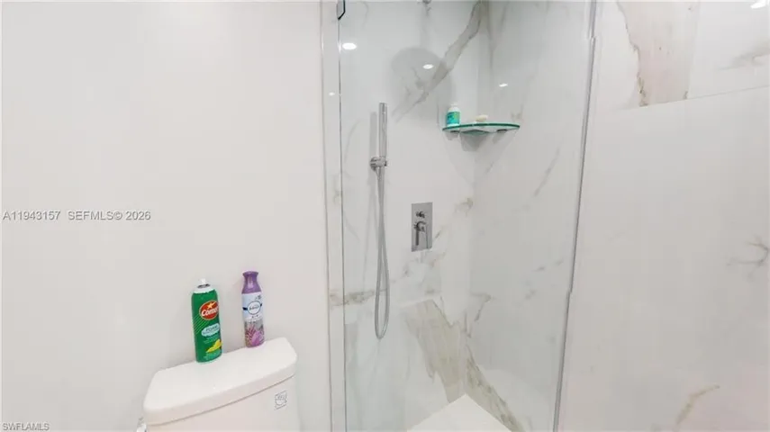 Shower enclosure with white and grey variegated wall tile, clear glass partition, and a wall-mounted showerhead with handheld sprayer