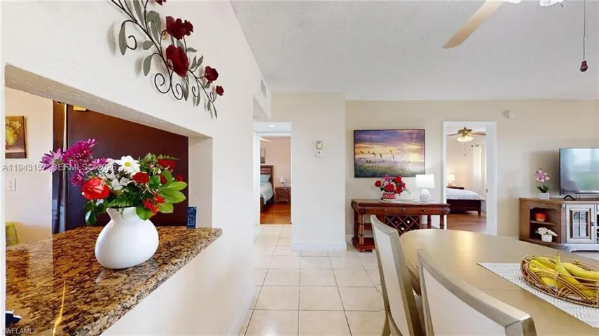 Open-concept living area featuring a pass-through window with a granite-style countertop, neutral wall tones, and square floor tiles