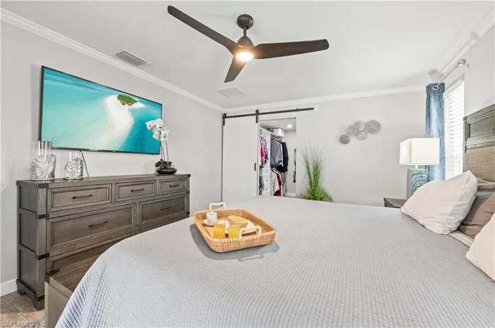 Primary Bedroom featuring a barn door, ceiling fan, and ornamental molding