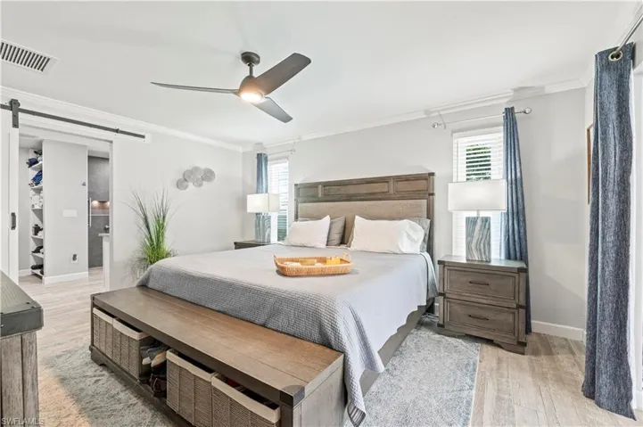 Primary Bedroom with ceiling fan, a barn door, light wood-type flooring, and multiple windows