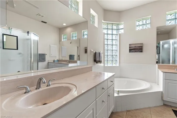 Bathroom with tile floors, tiled tub, vanity, and ceiling fan