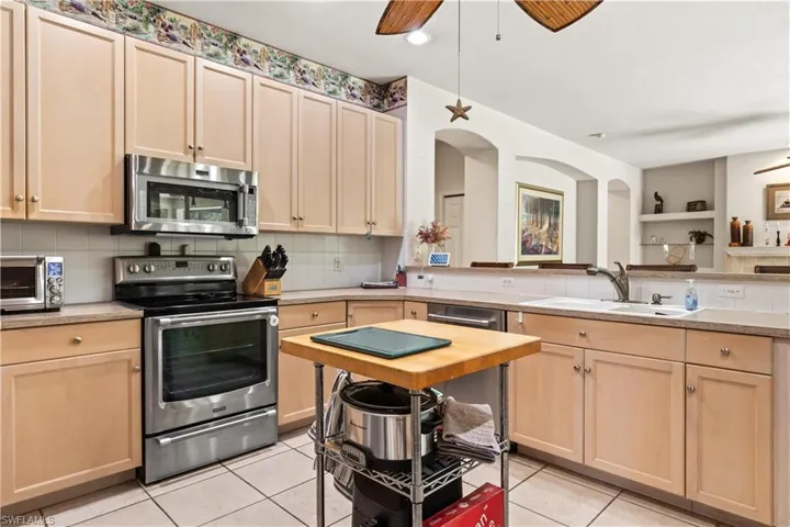 Kitchen with appliances with stainless steel finishes, sink, tasteful backsplash, ceiling fan, and light tile floors