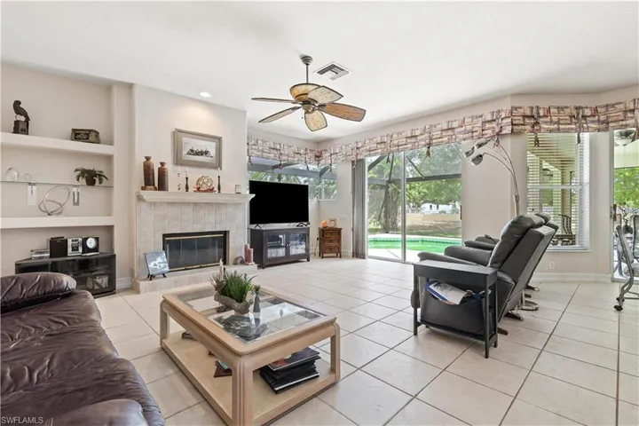 Living room featuring light tile floors, ceiling fan, a tile fireplace, and built in shelves