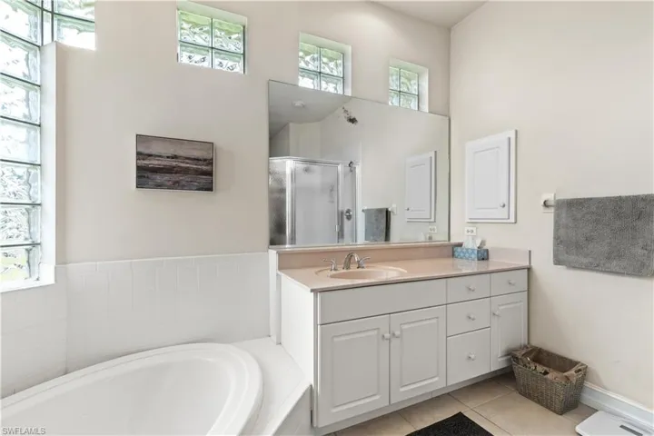 Bathroom with tile floors, independent shower and bath, a towering ceiling, and vanity with extensive cabinet space