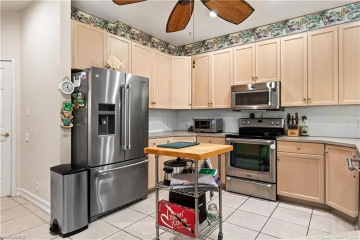 Kitchen featuring ceiling fan, stainless steel appliances, light tile flooring, and light brown cabinetry