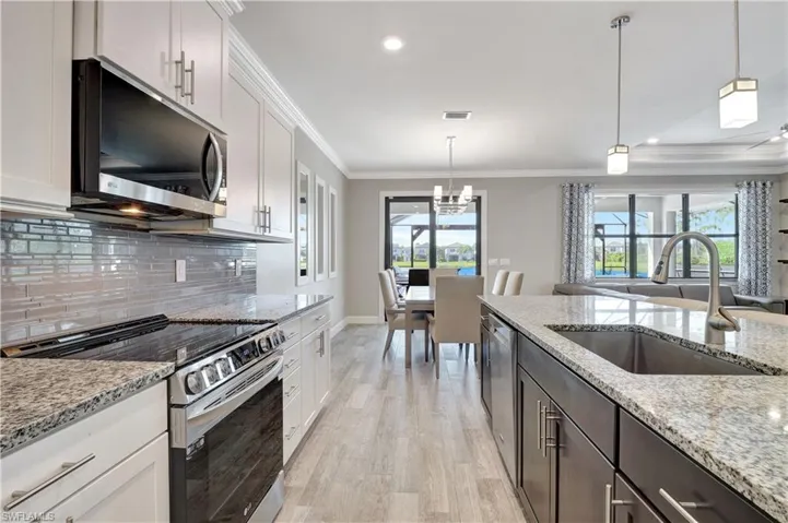 Kitchen featuring light hardwood / wood-style flooring, decorative light fixtures, appliances with stainless steel finishes, white cabinetry, and decorative backsplash