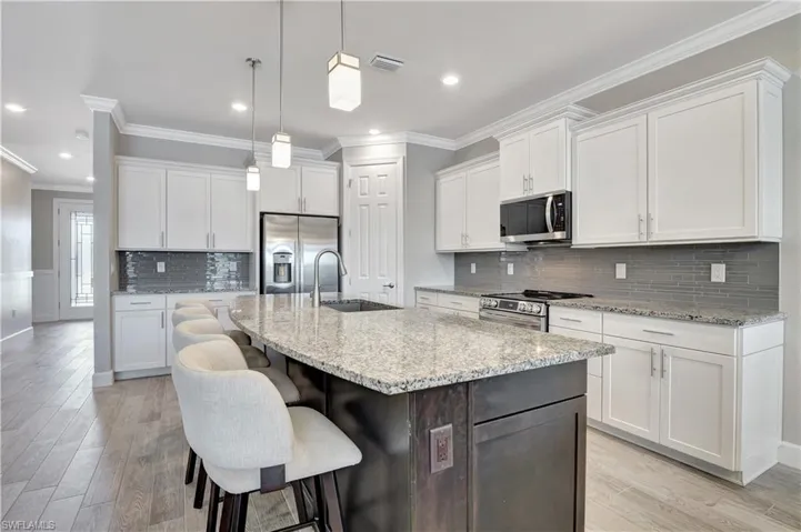 Kitchen featuring white cabinets, stainless steel appliances, a center island with sink, and crown molding