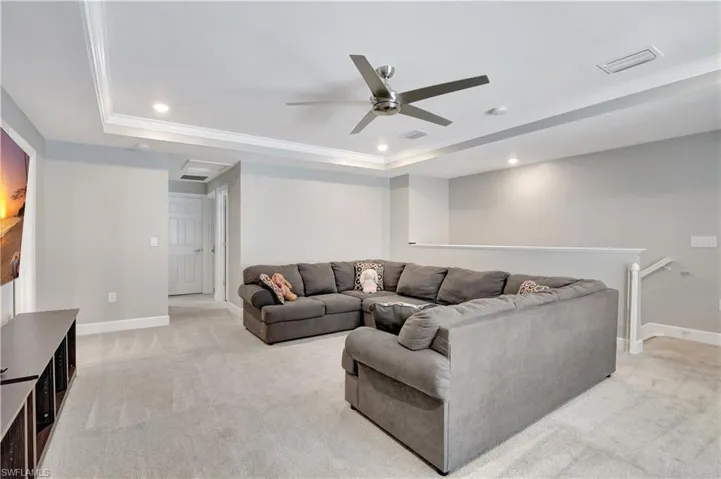 Carpeted living room with ceiling fan, ornamental molding, and a tray ceiling