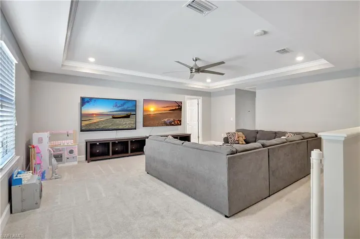 Living room with ceiling fan, light colored carpet, and a raised ceiling
