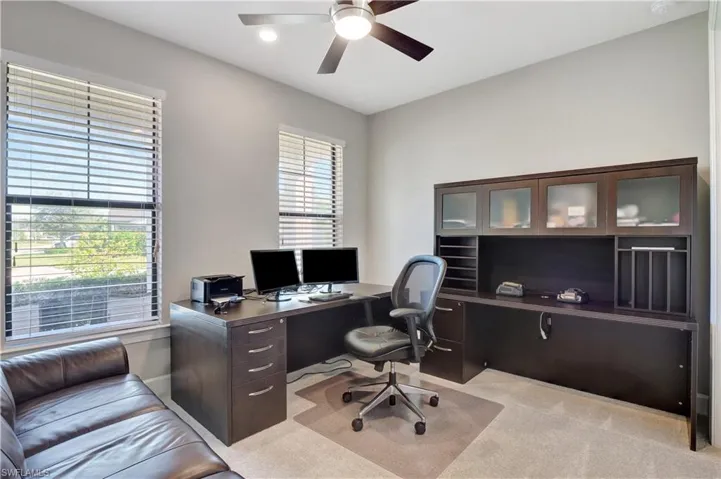 Carpeted home office with plenty of natural light and ceiling fan