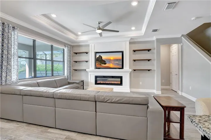 Living room with ceiling fan, ornamental molding, a raised ceiling, and light hardwood / wood-style flooring