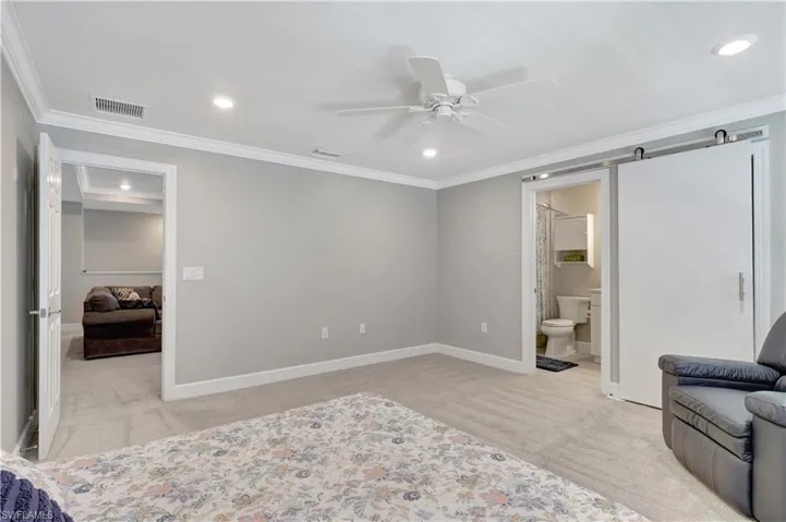 3rd Bedroom with ensuite bath, a barn door, light carpet, ceiling fan, and ornamental molding