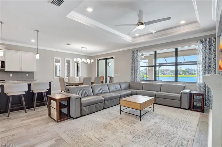 Living room featuring ceiling fan with notable chandelier, a raised ceiling, light hardwood / wood-style floors, and crown molding