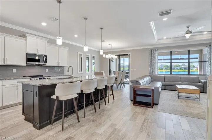 Kitchen with ceiling fan with notable chandelier, light stone countertops, a breakfast bar area, a center island with sink, and white cabinets