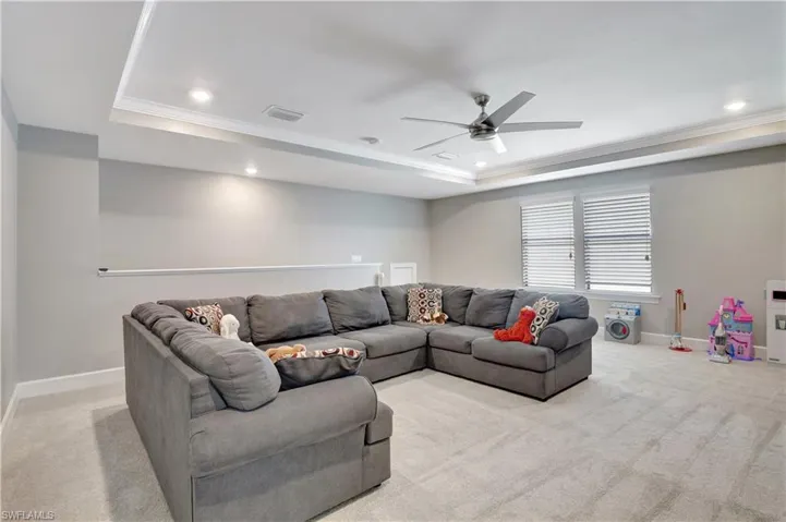 Carpeted living room with ceiling fan, a raised ceiling, and crown molding