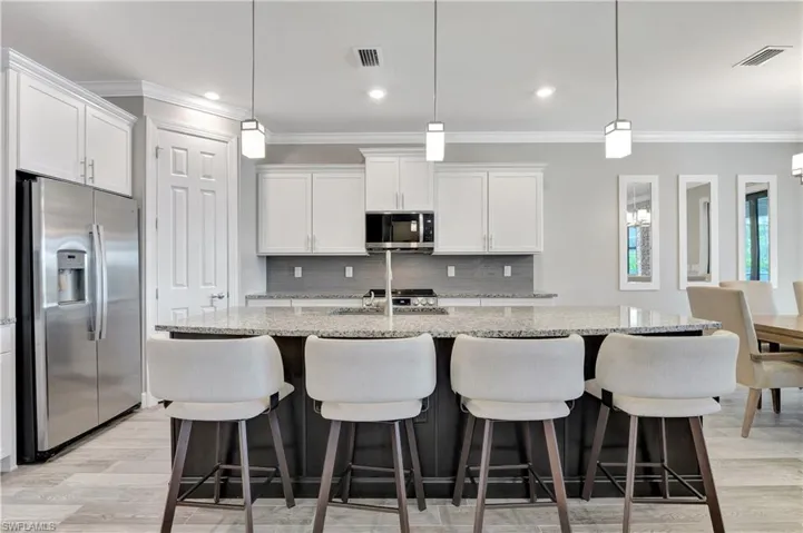 Kitchen featuring appliances with stainless steel finishes, a center island with sink, white cabinetry, and a breakfast bar