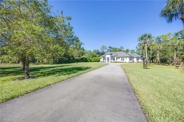 Huge front lawn with open space and shade trees, house set back from the road with long driveway.