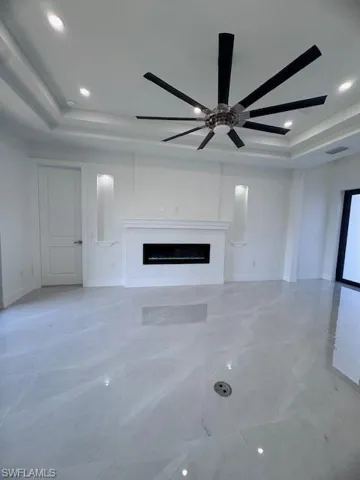 Unfurnished living room featuring a fireplace, a raised ceiling, and ceiling fan