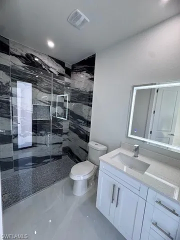 Bathroom featuring vanity, a shower with door, and toilet