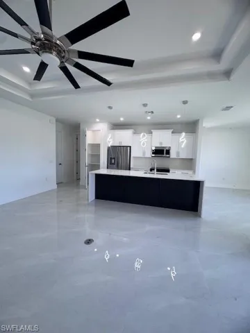 Kitchen with white cabinetry, a large island with sink, a raised ceiling, and stainless steel refrigerator