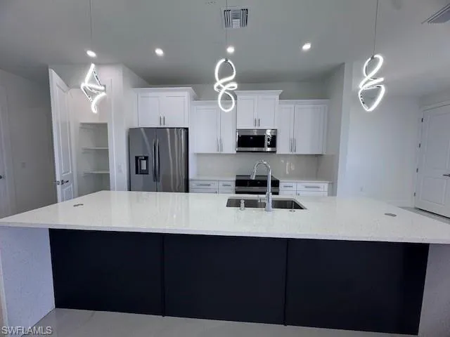 Kitchen with decorative light fixtures, refrigerator, sink, and a large island with sink