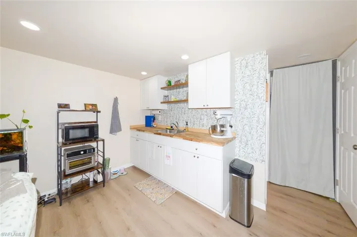 Kitchen featuring open shelves, white cabinets, light wood finished floors, black microwave, and recessed lighting