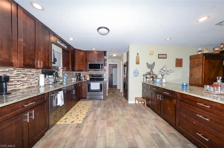 Kitchen with stainless steel appliances, light stone counters, light wood finished floors, dark wood finish cabinets, and recessed lighting