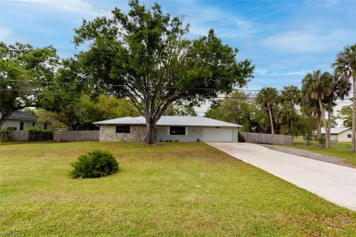 Ranch-style house featuring a garage, driveway, stone siding, and a metal roof
