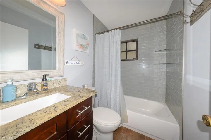 Full bathroom with vanity, shower / bathtub combination with curtain, and dark wood-style floors