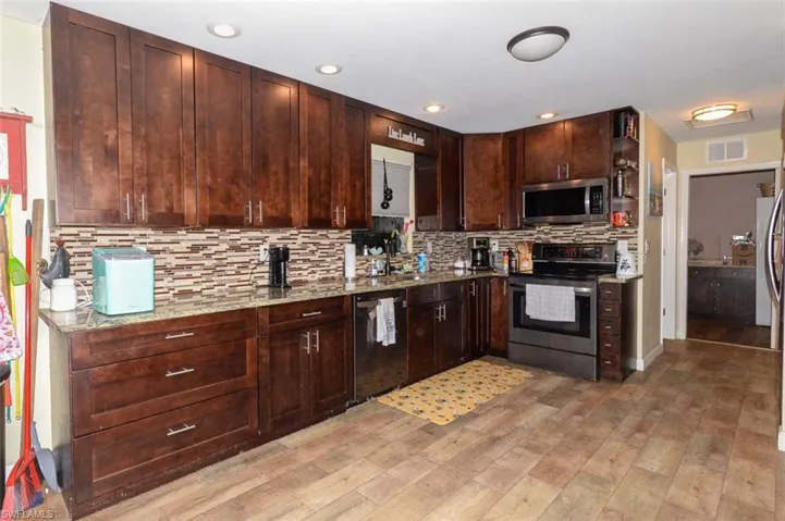Kitchen featuring stainless steel appliances, dark wood finish cabinets, light wood finished floors, light stone countertops, and backsplash