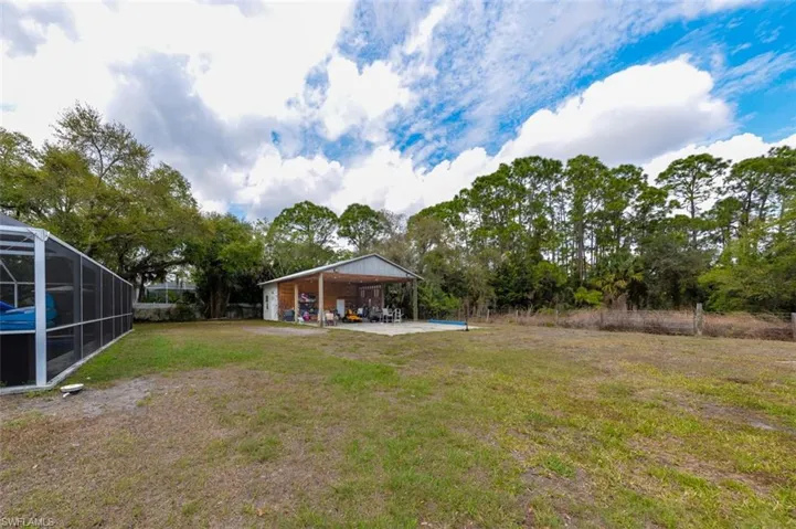 View of green lawn with a patio area and view of wooded area