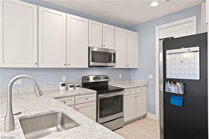 Kitchen featuring white cabinets, a sink, stainless steel appliances, and light stone countertops