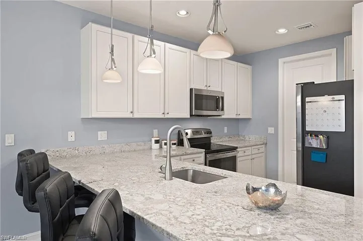Kitchen with a sink, light stone countertops, appliances with stainless steel finishes, and pendant lighting