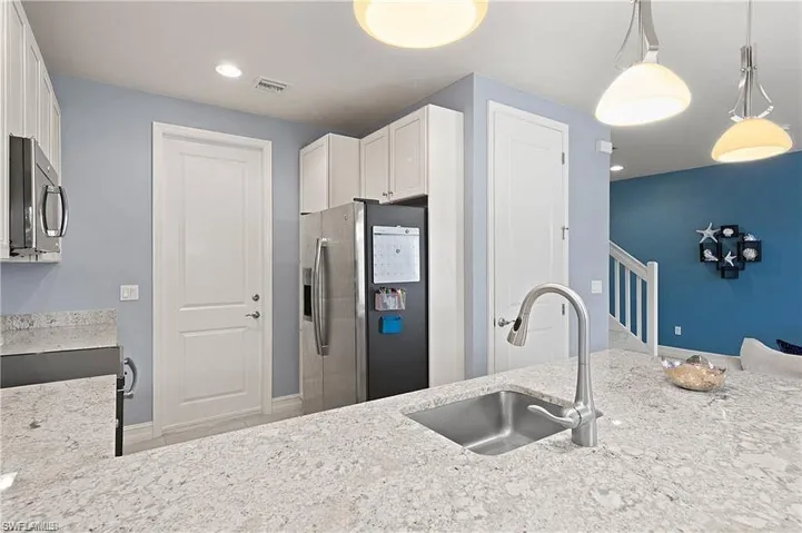 Kitchen with a sink, light stone countertops, appliances with stainless steel finishes, and pendant lighting