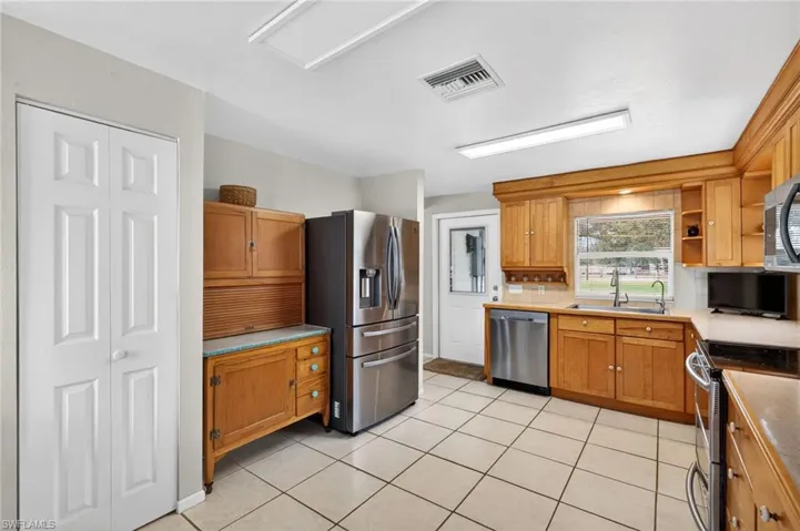Kitchen with stainless steel appliances, wood finish cabinetry, light countertops, light tile patterned floors, and open shelves