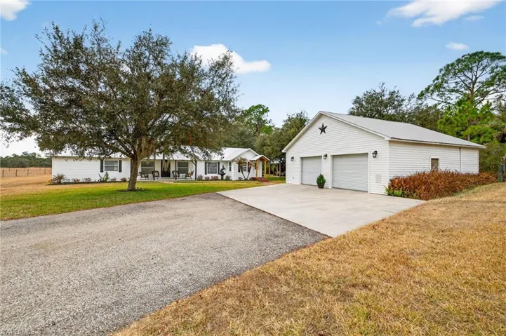 Single story home featuring a front lawn, a detached garage, driveway, and an outbuilding