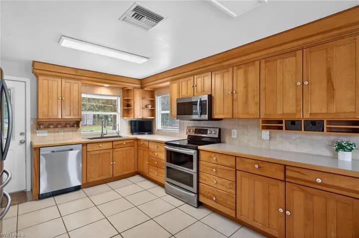 Kitchen featuring open shelves, stainless steel appliances, wood finish cabinetry, backsplash, and light tile patterned flooring