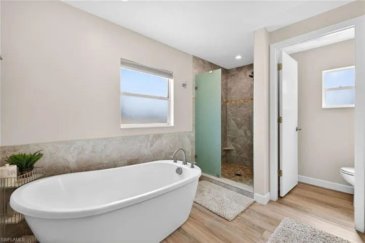 Bathroom featuring a freestanding bath, a shower stall, light wood-style flooring, and tile walls