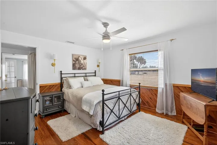 Bedroom with wainscoting, wood finished floors, wooden walls, and ceiling fan