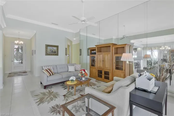 Living area featuring ceiling fan with notable chandelier, light tile patterned floors, and ornamental molding