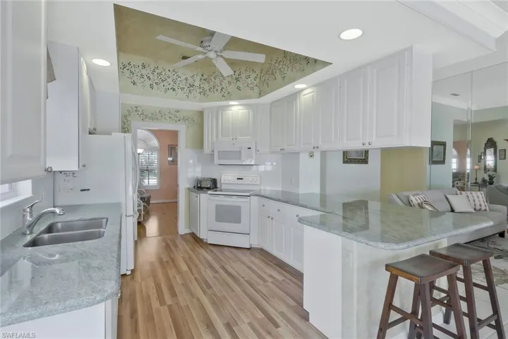 Kitchen featuring white appliances, a tray ceiling, a peninsula, a ceiling fan, and a sink